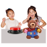 Two young girls smiling and playing with an adaptive switch for a teddy bear