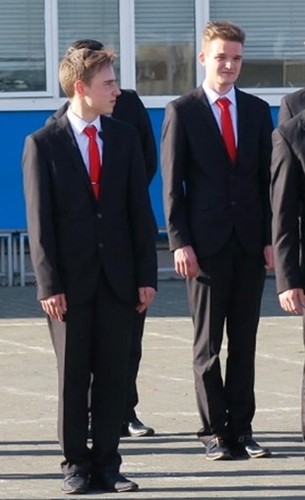 two young people wearing black school blazers and red ties