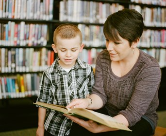 Teacher helps young boy to read a book